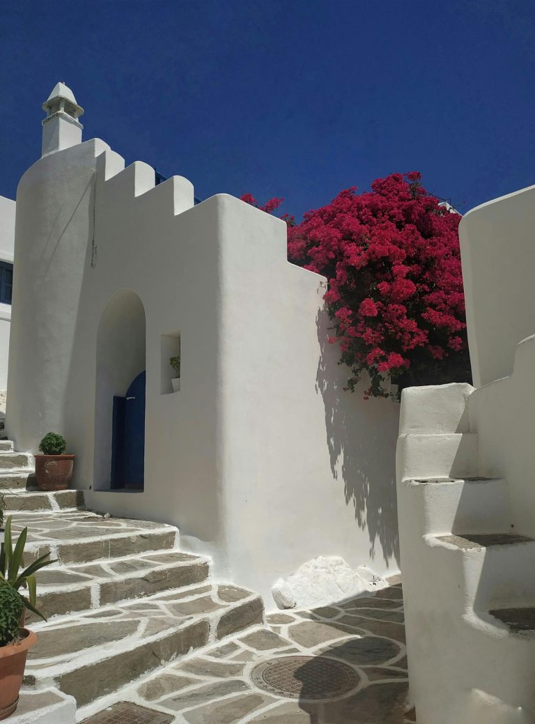 Greek architecture with vibrant bougainvillea under sunny blue sky.