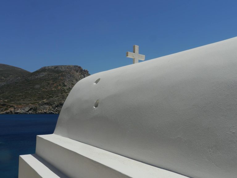 Serene view of a traditional white dome and cross by the Aegean Sea in Greece under a clear blue sky.