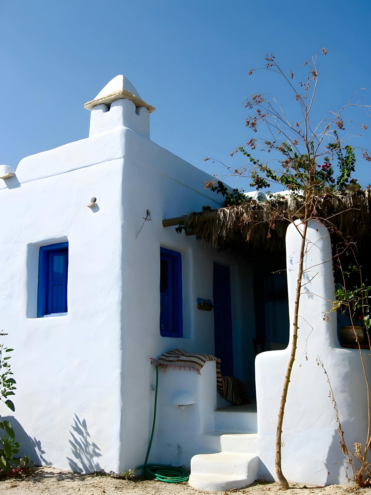 Traditional Cycladic house with white walls and striking blue windows under a clear sky.